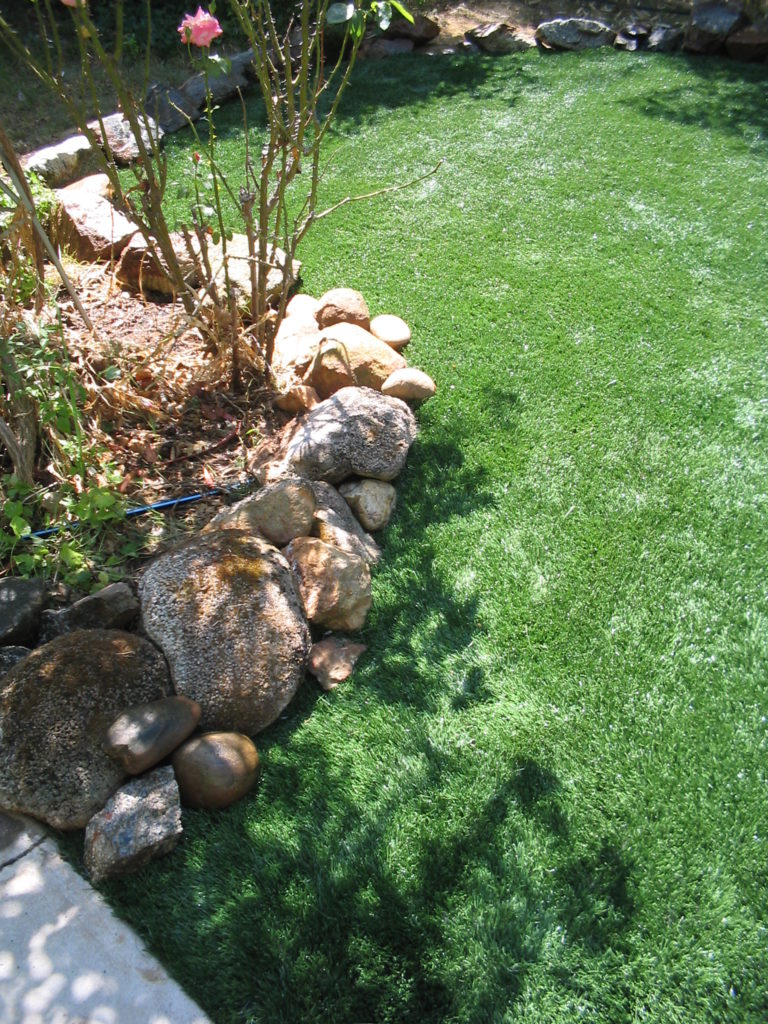 The large rock trim used for this garden edge replaces the need for bender board along the edge of this artificial grass lawn area.